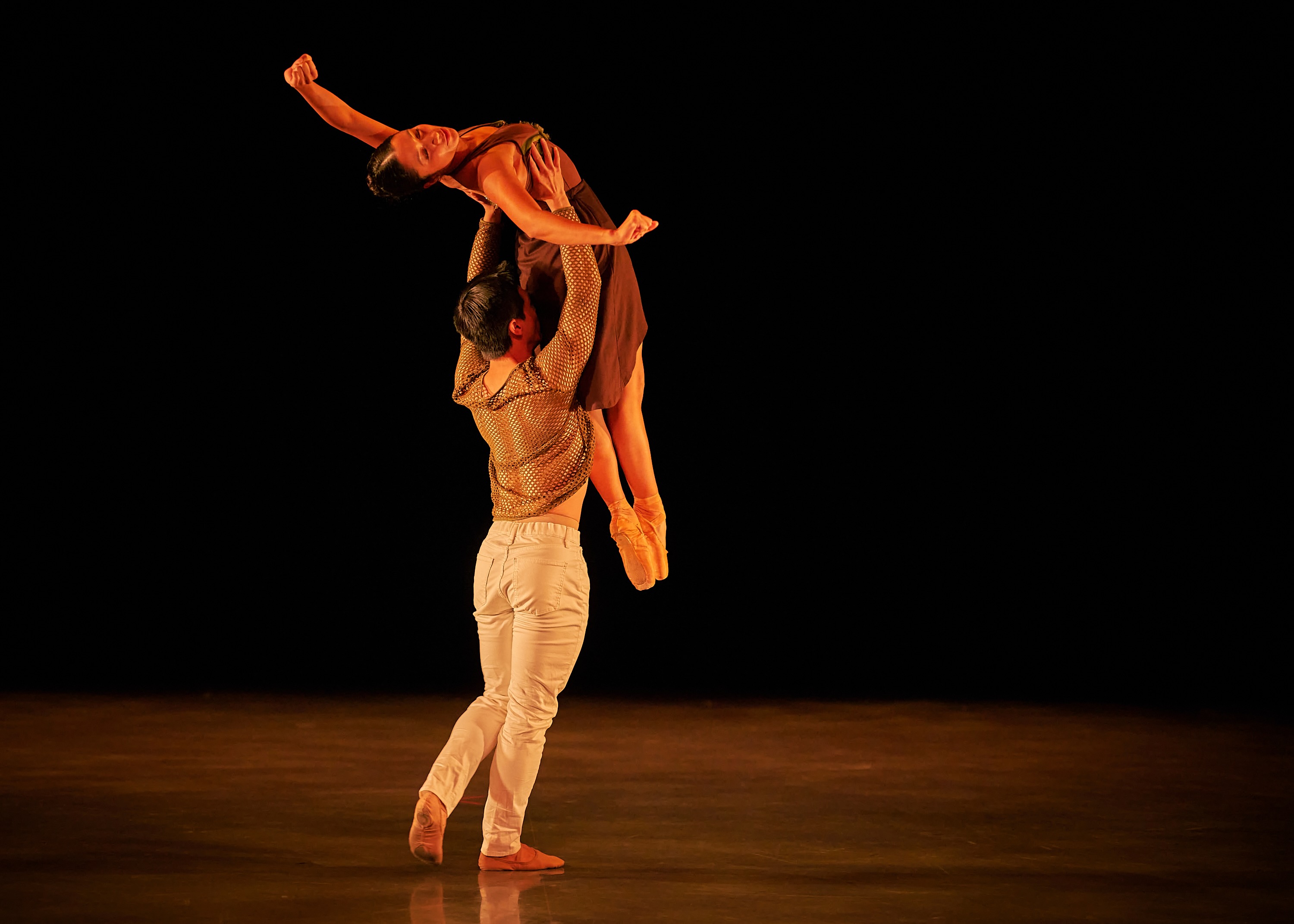 A dancer holds his partner in a high, extended overhead lift.