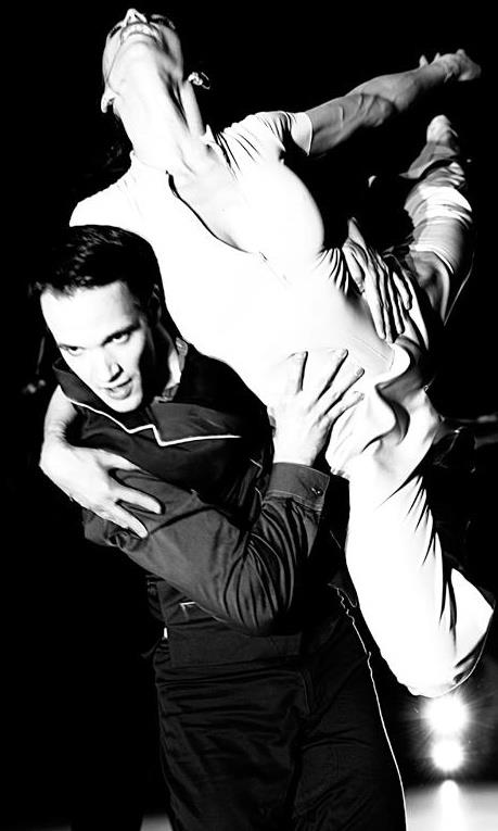 Ian Parsons supports a partner overhead in a black-and-white ballet performance photograph.