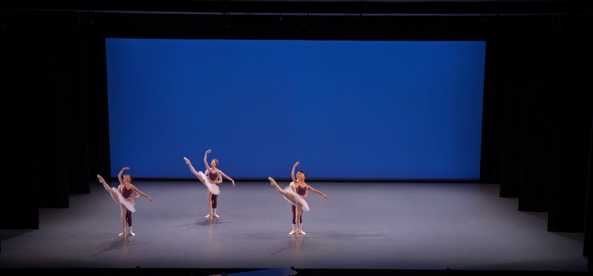 Advanced ballet students demonstrate partnered movement on a blue-lit stage.