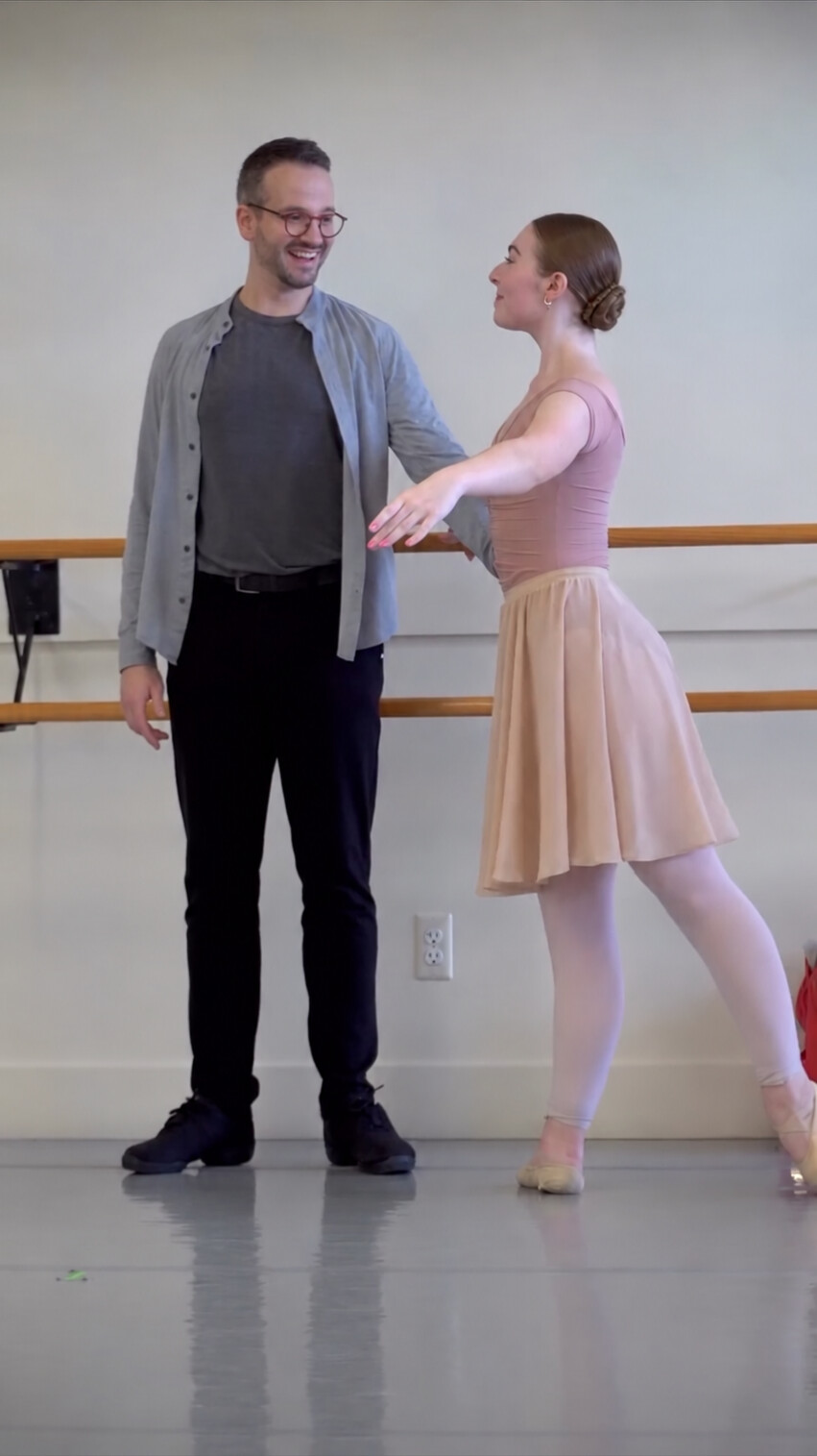 Ian Parsons and a ballet student smile at one another while working together beside the studio barre.